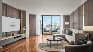Habitación de hotel moderna con un televisor grande, un sofá, una mesa de centro y vistas panorámicas de la ciudad a través de amplias ventanas.