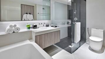 Een moderne badkamer met een bad, een douche en een toilet. Handdoeken en toiletartikelen liggen op het aanrecht.