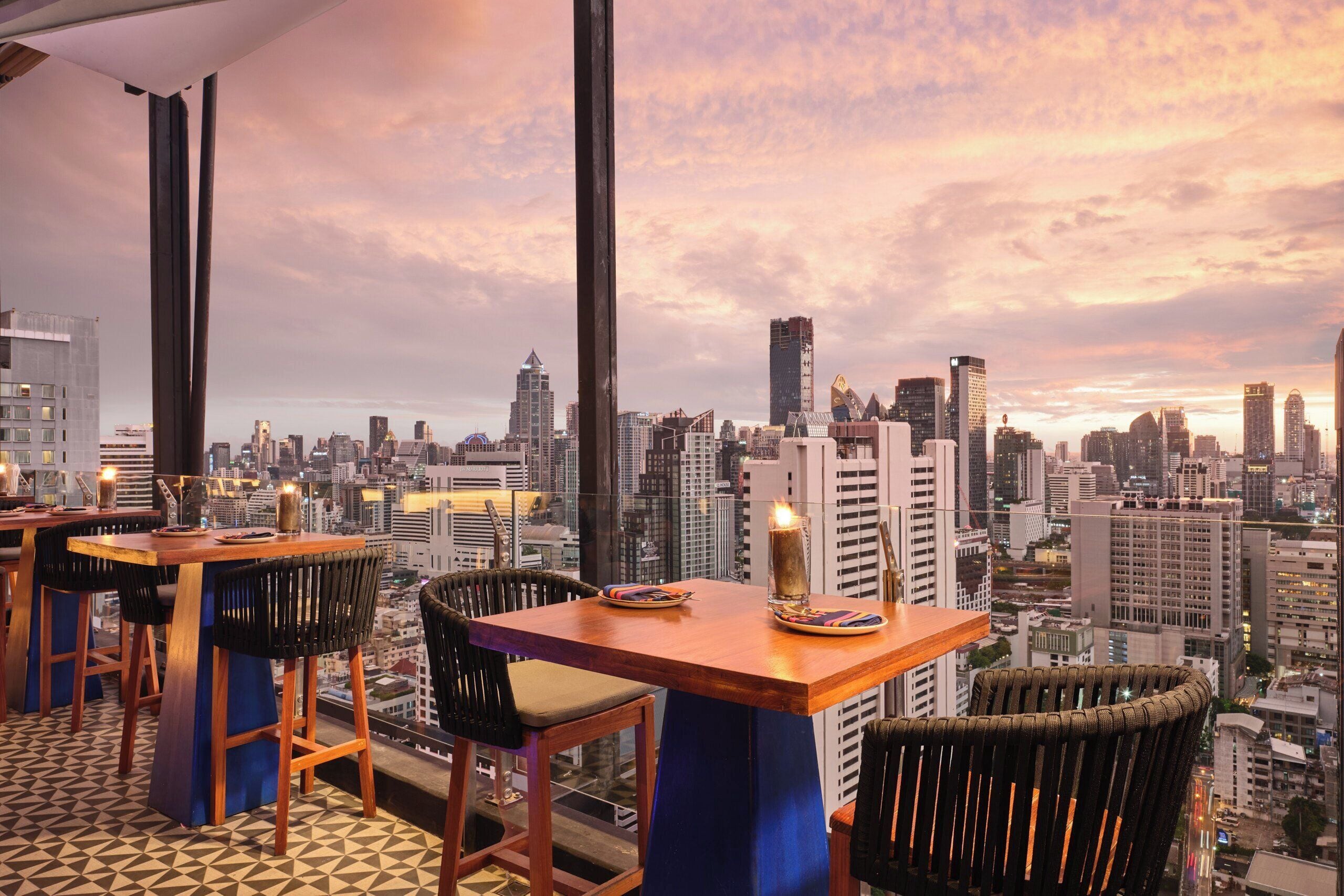 Eine Bar in einem Hochhaus mit Blick auf die Stadt, ausgestattet mit moderner Möbel und einem großen Fenster.