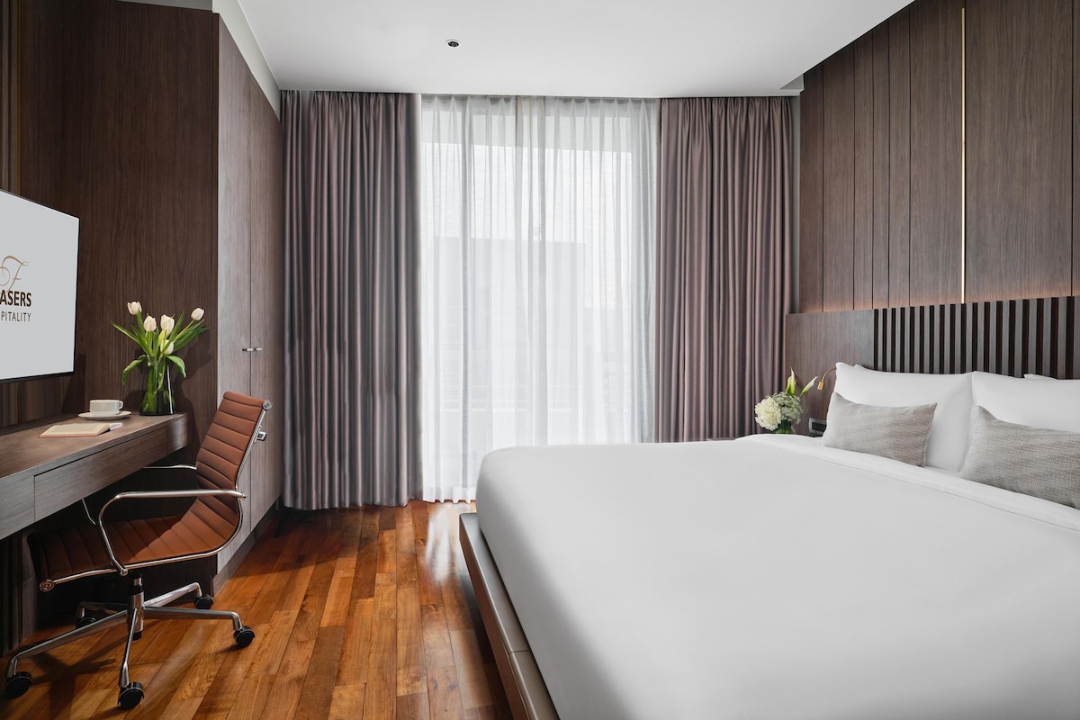 A hotel room with a large bed, a desk with a chair, a television, and a window with curtains.