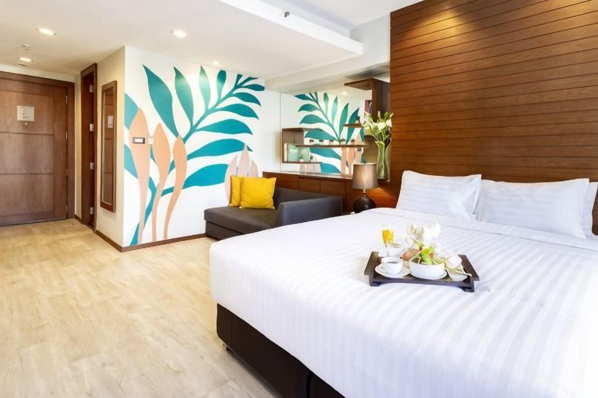 A hotel room with a large bed, a wooden headboard, a desk with a chair, and a wall with a leaf pattern.