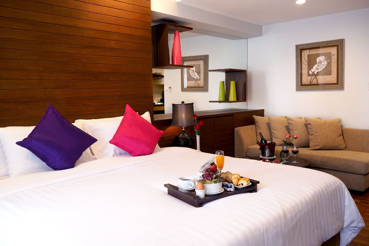 Ein Hotelzimmer mit Bett, Sofa, Tablett mit Frühstücksgegenständen und Bildern an den Wänden.