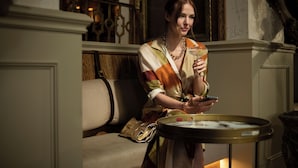 A woman sitting on a sofa with a drink in her hand and a handbag beside her. - De Vere Beaumont Estate (Windsor)
