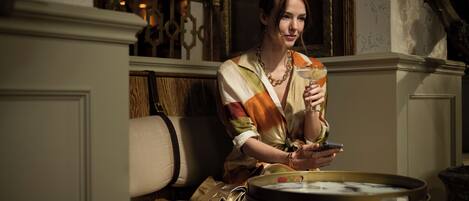 A woman sitting on a sofa with a drink in her hand and a handbag beside her.