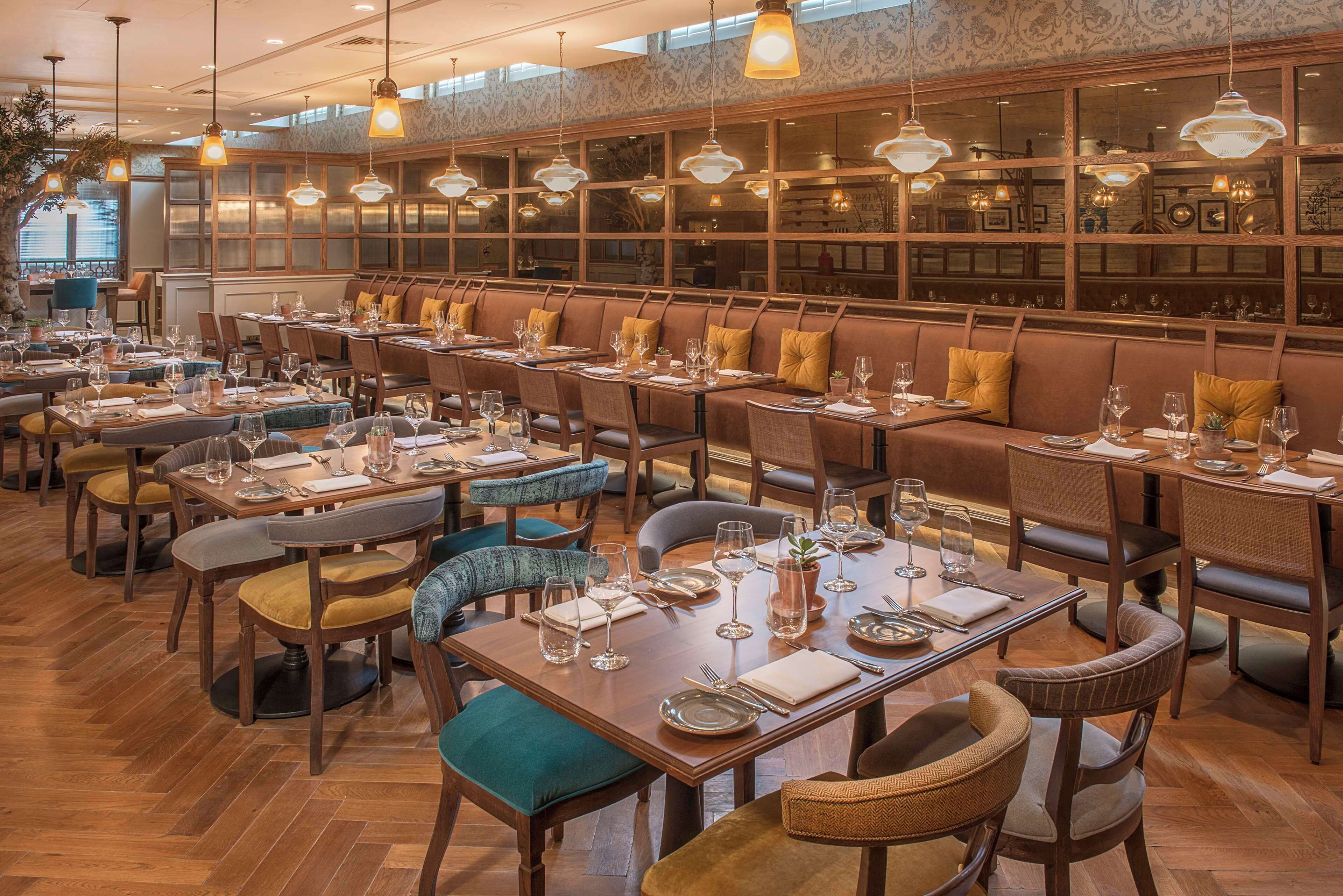 A restaurant with multiple dining tables and booths, wooden flooring, and hanging pendant lights.