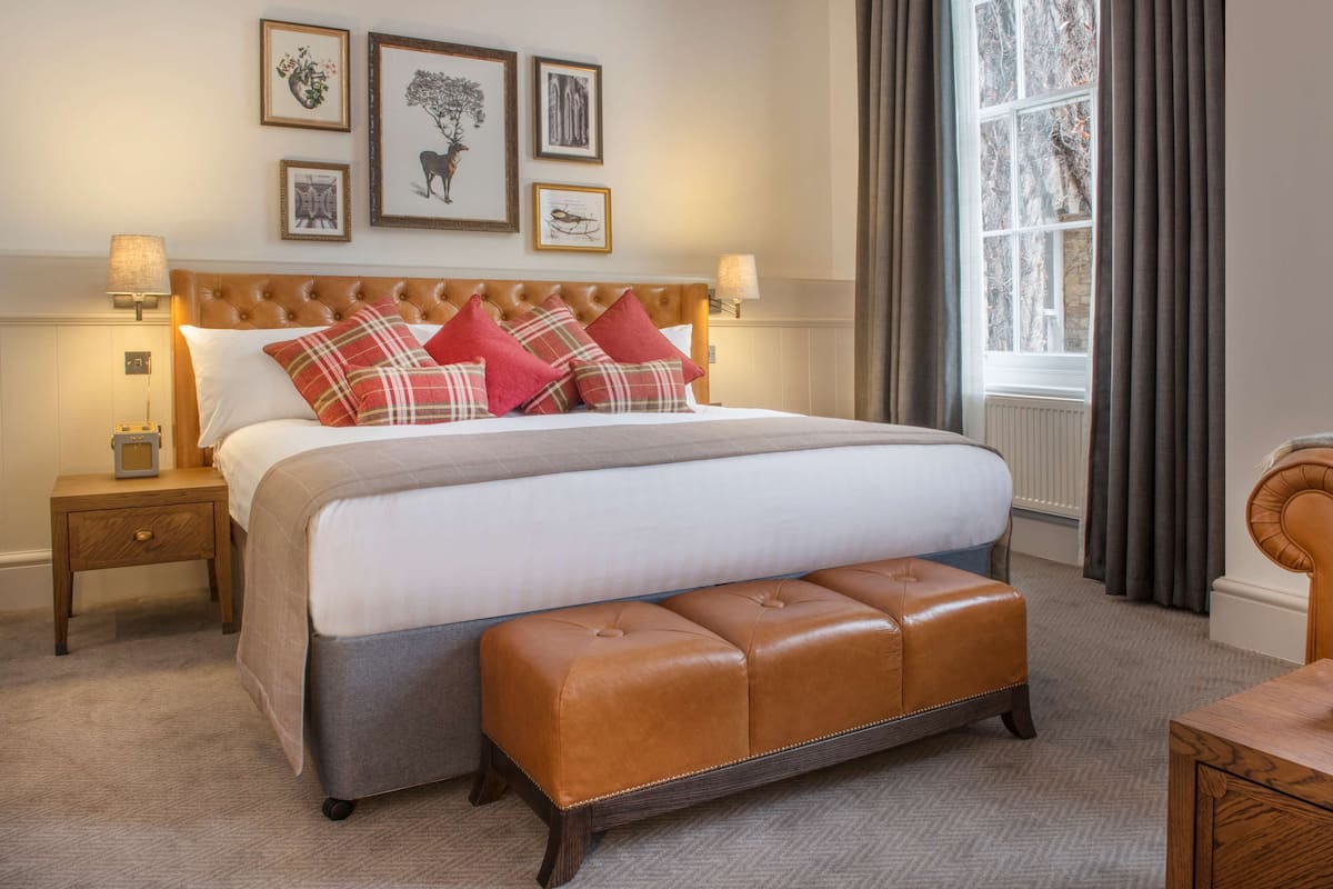 A neatly arranged bedroom with a large bed, a wooden bench, and framed artwork on the wall.