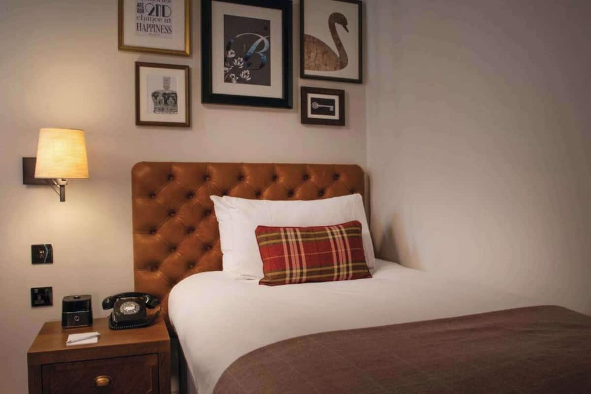 A neatly made bed with a brown headboard, a bedside lamp, a telephone, and framed pictures on the wall.