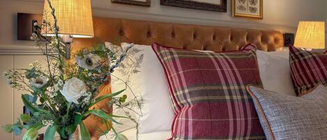 A bedroom with a tufted headboard, a bed with white linens, and a floral arrangement on a nightstand.