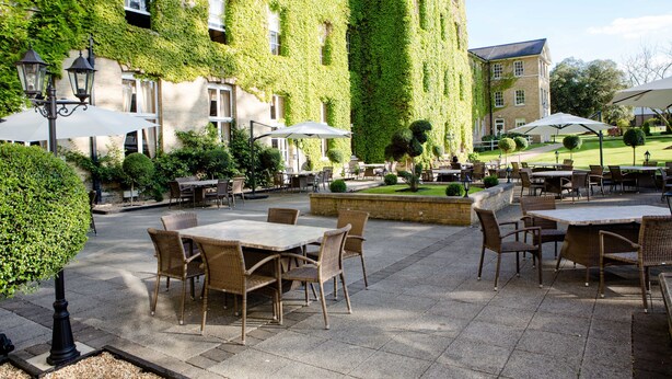 An outdoor patio with tables and chairs, surrounded by a building with ivy-covered walls. - De Vere Beaumont Estate (Windsor)