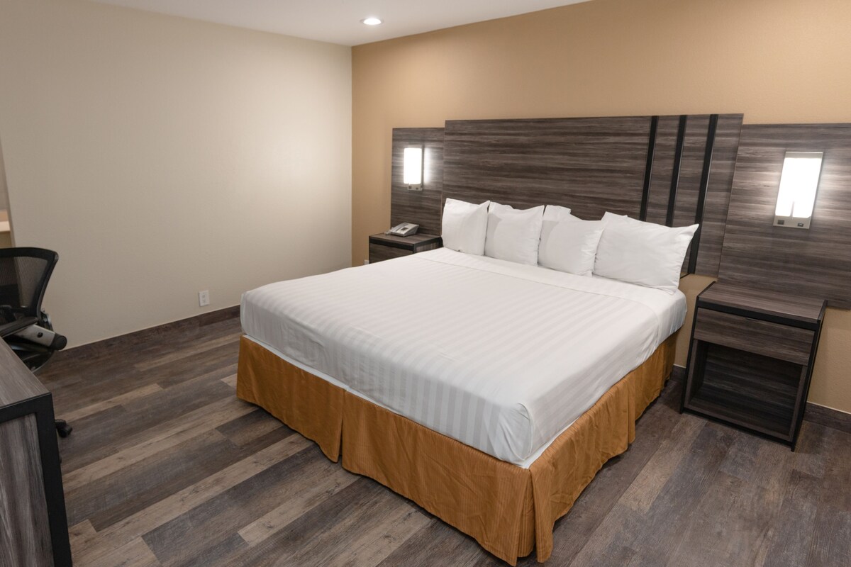Habitación de hotel con una cama grande, un escritorio, una silla, una mesita de noche y una lámpara fijada a la pared.
