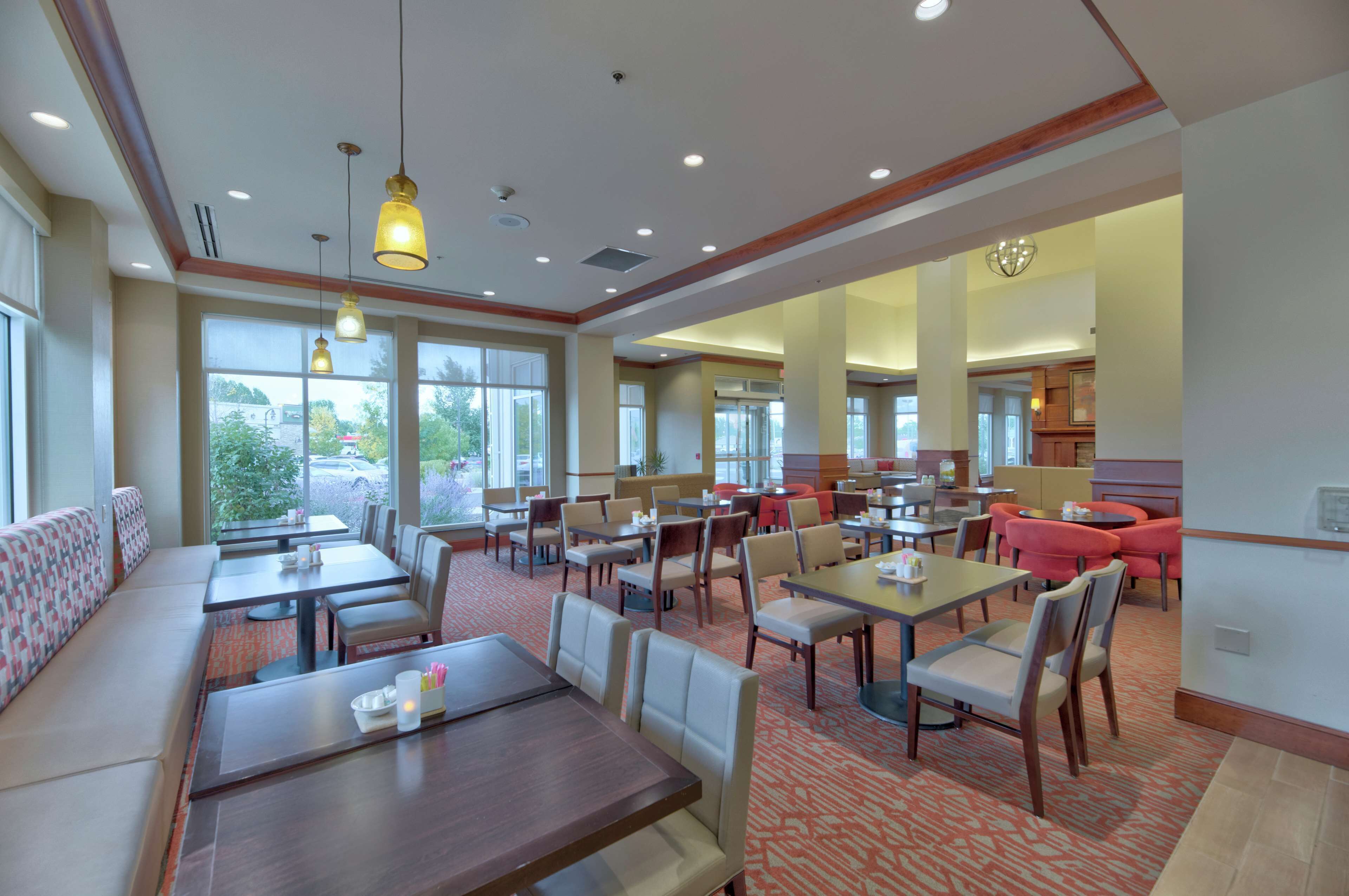 Un vaste espace dédié à la salle à manger, avec de nombreuses tables et chaises, de grandes fenêtres et une vue sur l’extérieur.