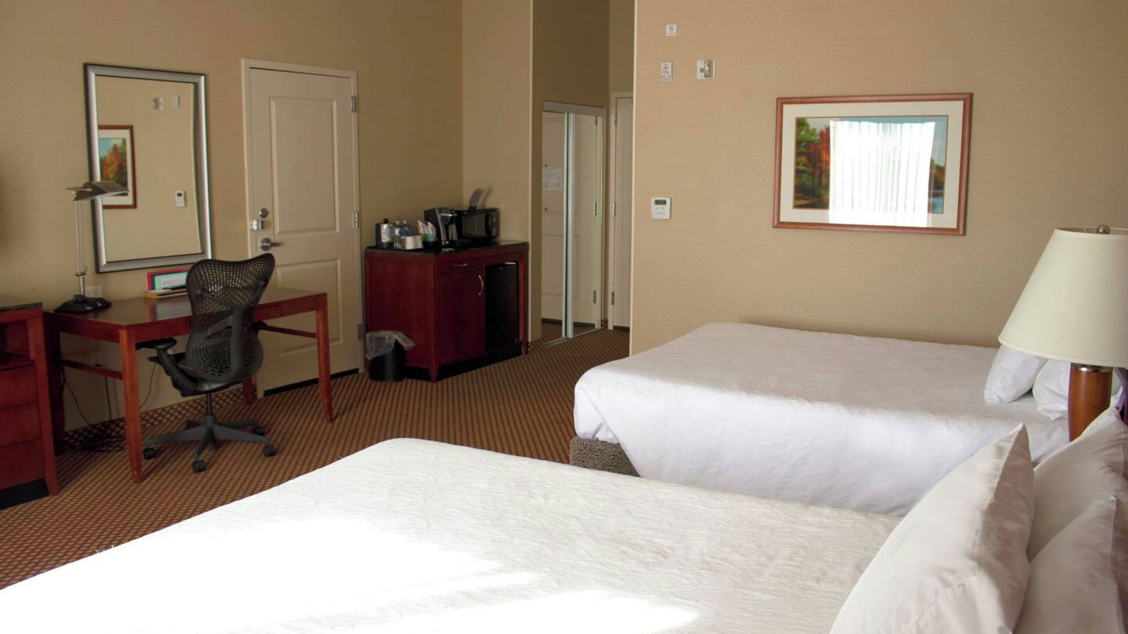 Habitación de hotel con dos camas, un escritorio, una silla, un aparador y un espejo.