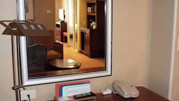 Una habitación de hotel con escritorio, teléfono, espejo y un cartel que indica que la habitación pertenece al hotel Hilton Garden Inn PROMISE.