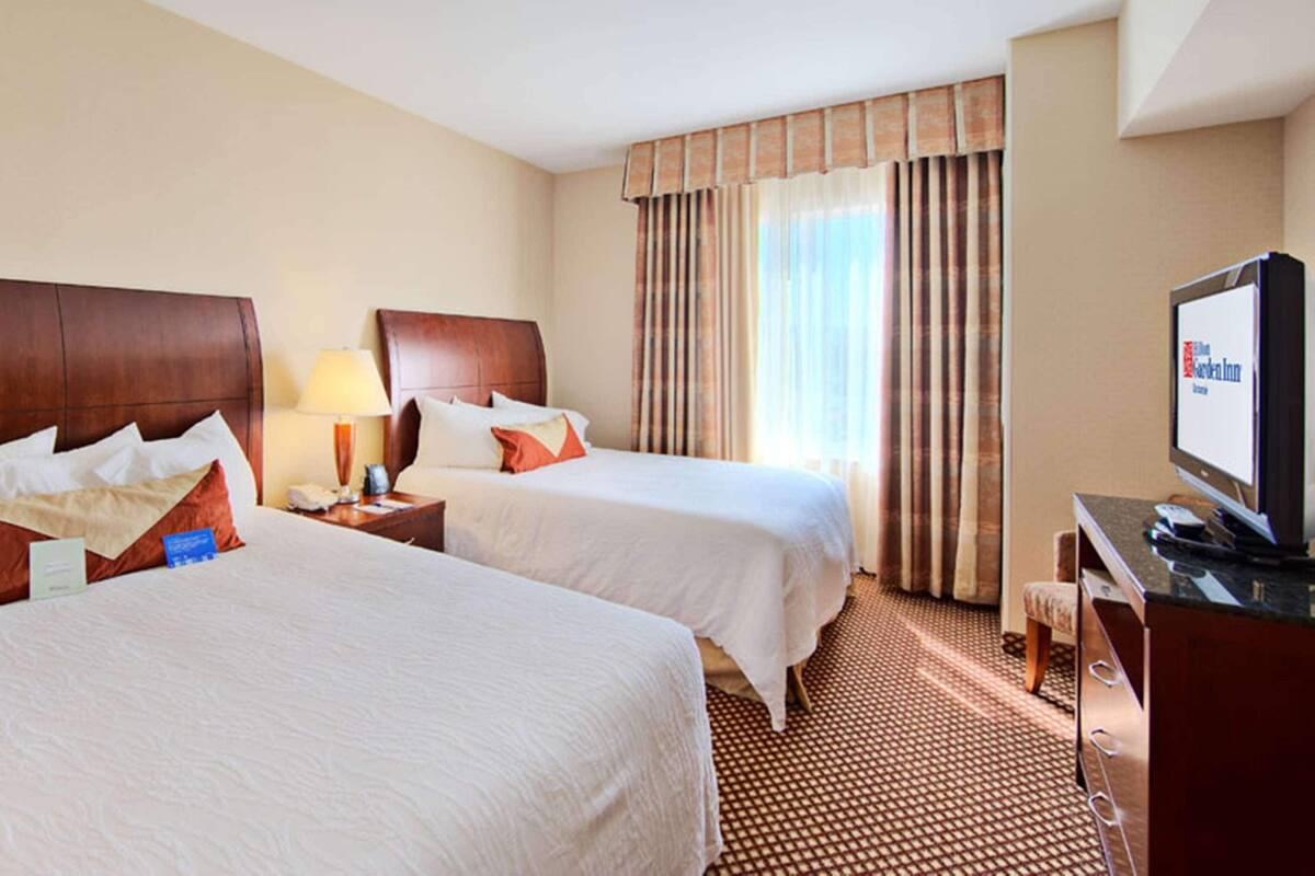Une chambre d’hôtel avec deux lits, une télévision, un bureau et une fenêtre avec des rideaux.