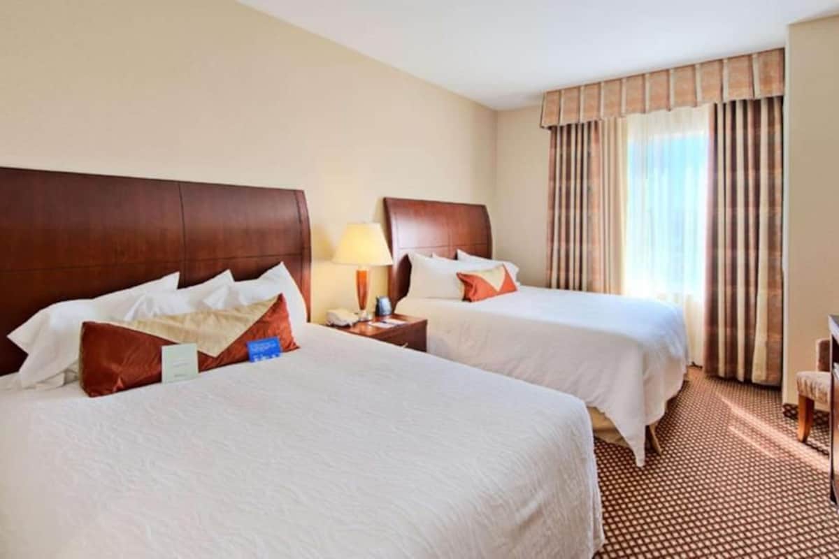A hotel room with two beds, a television, a desk, and a window with curtains.