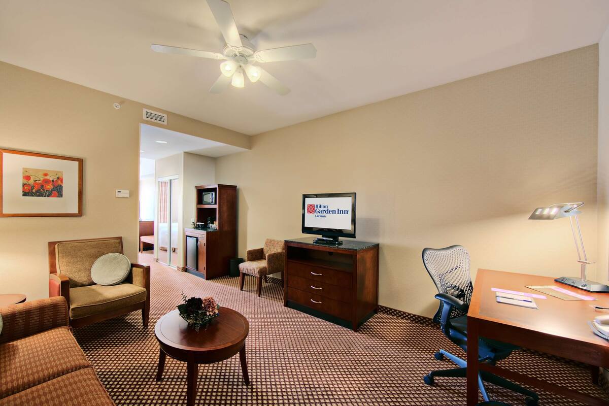 Une chambre d’hôtel équipée d’un lit, d’un bureau, d’une chaise, d’une télévision et d’un ventilateur de plafond.
