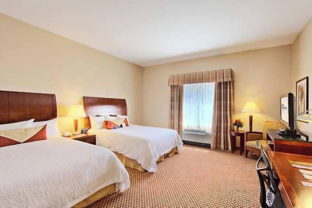 Une chambre d’hôtel avec deux lits, un bureau avec un ordinateur, une chaise et une fenêtre avec des rideaux.