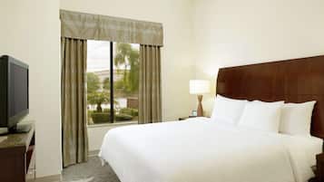 A hotel room with a large bed, a television on a stand, a nightstand with a lamp, and a window with curtains.
