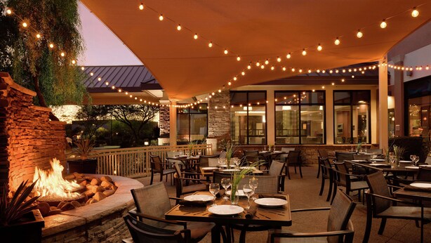 An outdoor dining area with tables and chairs, a fire feature, and string lights. - Hilton Garden Inn Phoenix North Happy Valley (Phoenix)