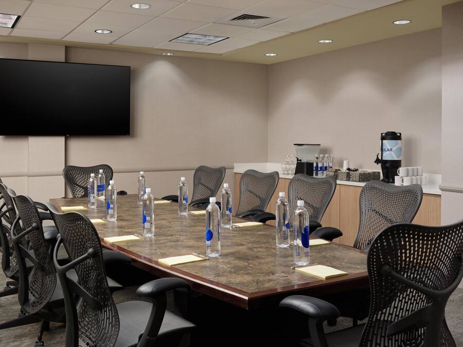 A conference room with a large flat-screen TV, a coffee station, and water bottles on the table.