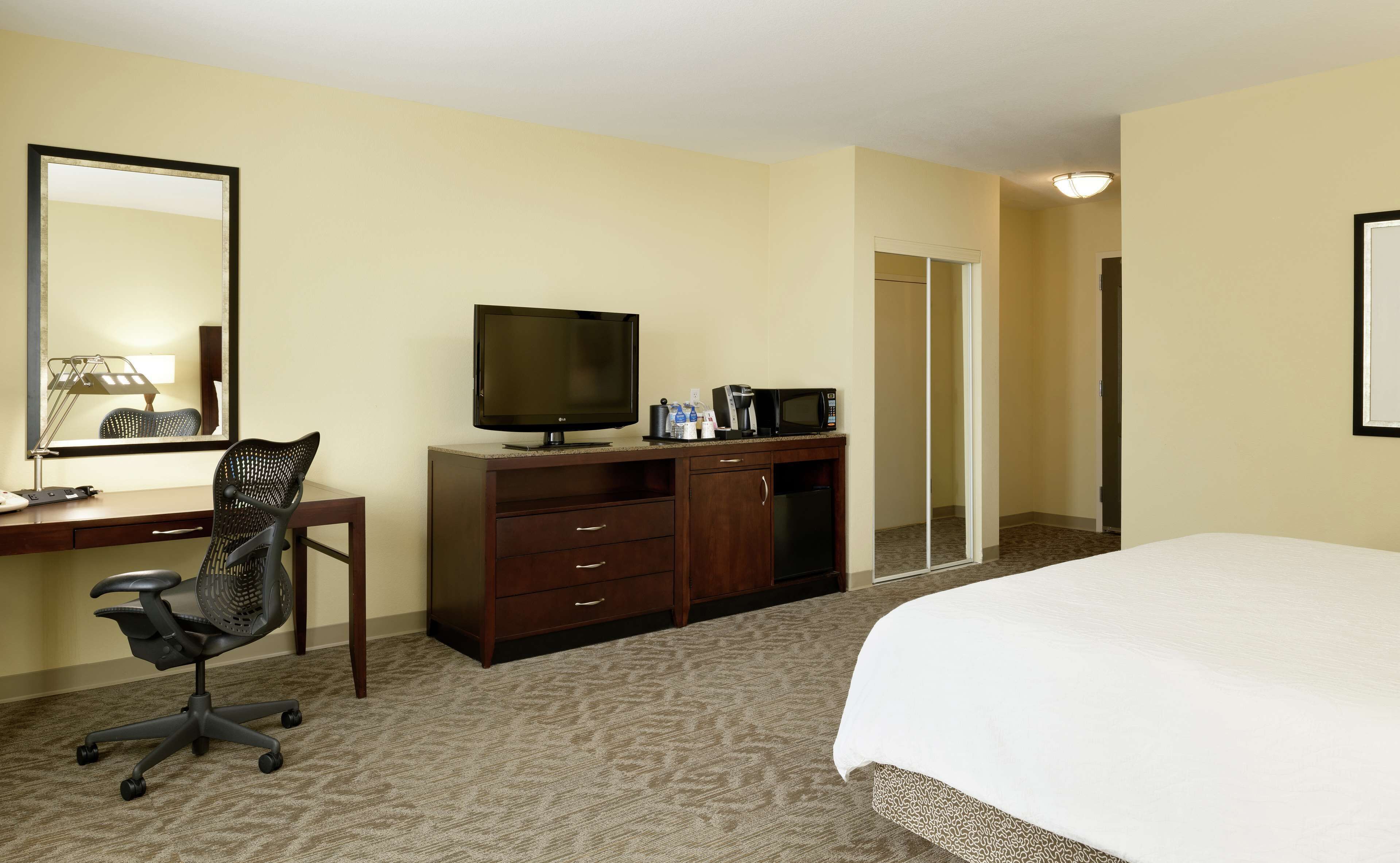 Habitación de hotel con cama, escritorio con computadora, silla, televisión, microondas y armario.