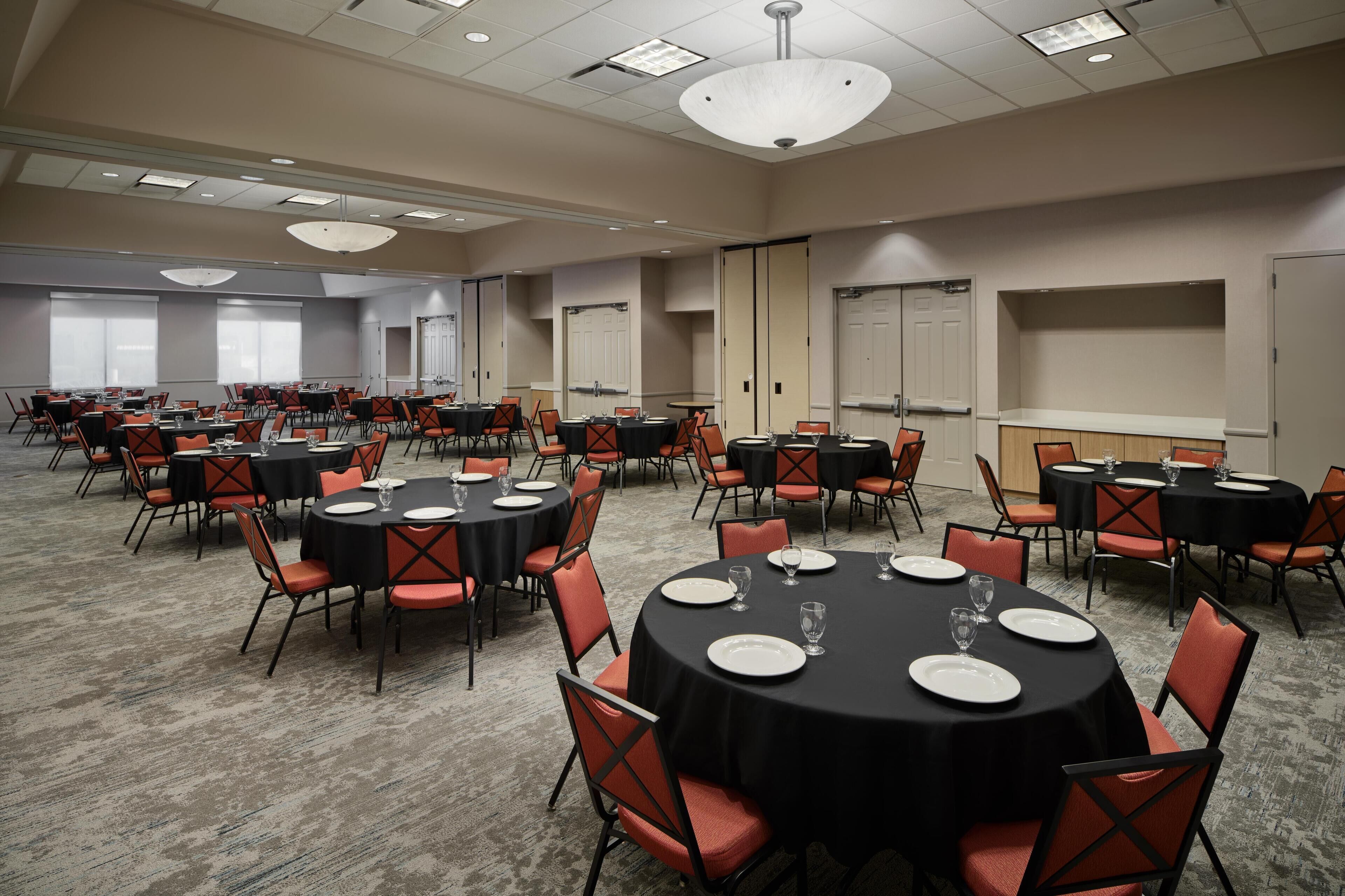 A large conference room with multiple round tables, each set with white plates and glasses, and orange chairs.