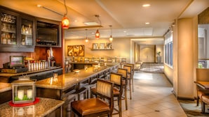 A hotel bar with a long counter, bar stools, and a television screen displaying the hotel name. - Hilton Garden Inn Phoenix North Happy Valley (Phoenix)