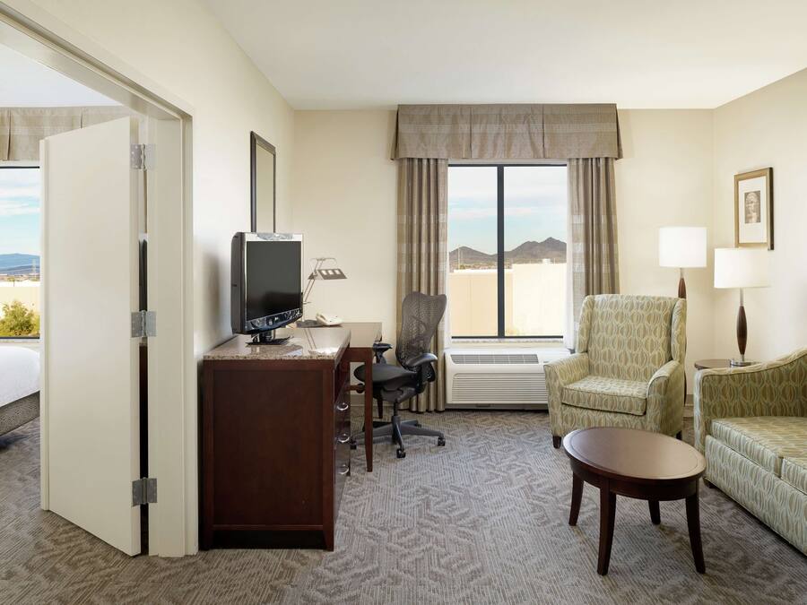 A hotel room with a bed, desk, TV, office chair, armchair, sofa, and a small table.