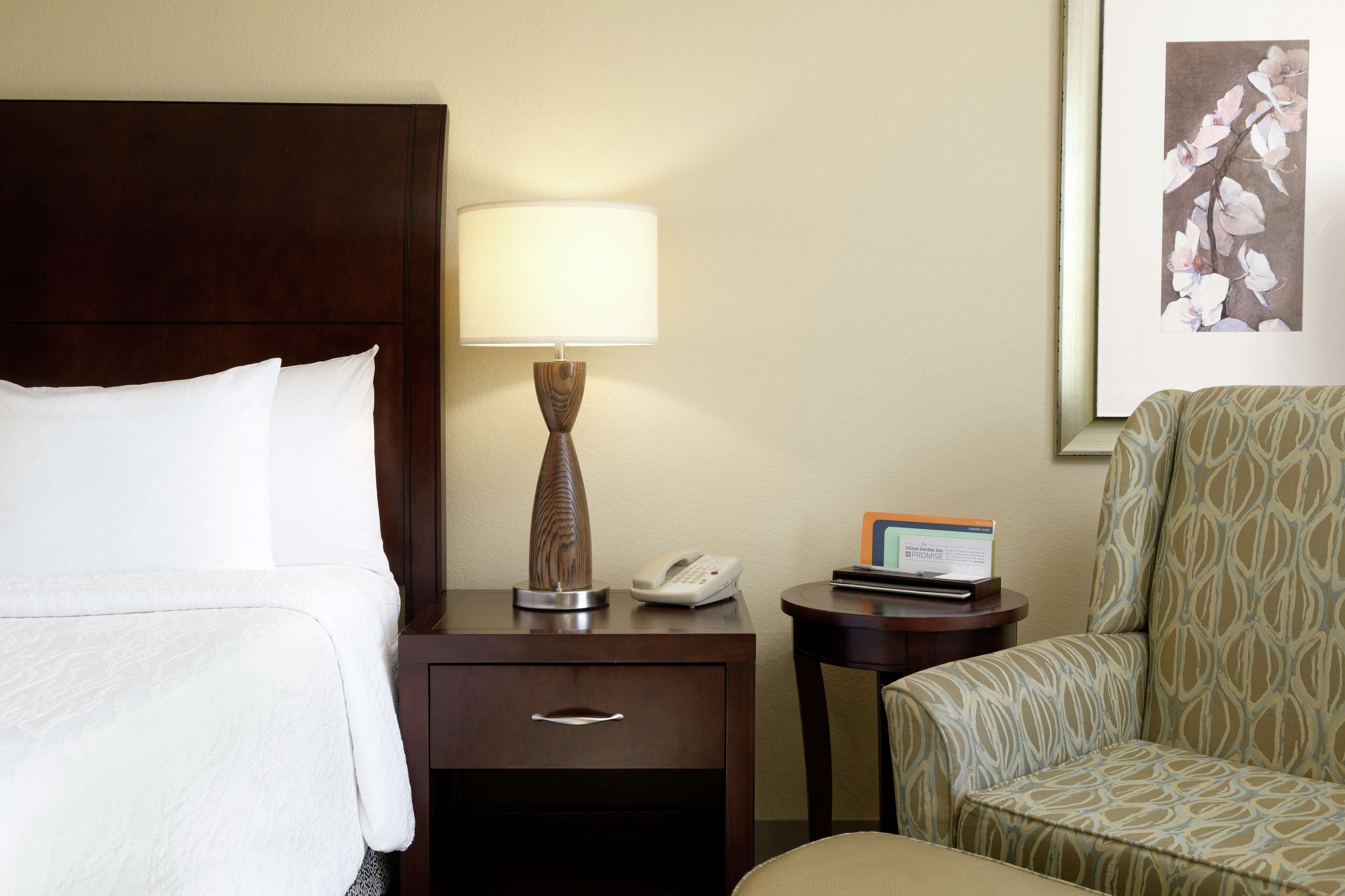 A hotel room with a bed, a nightstand with a lamp, a telephone, and a small table with a card.