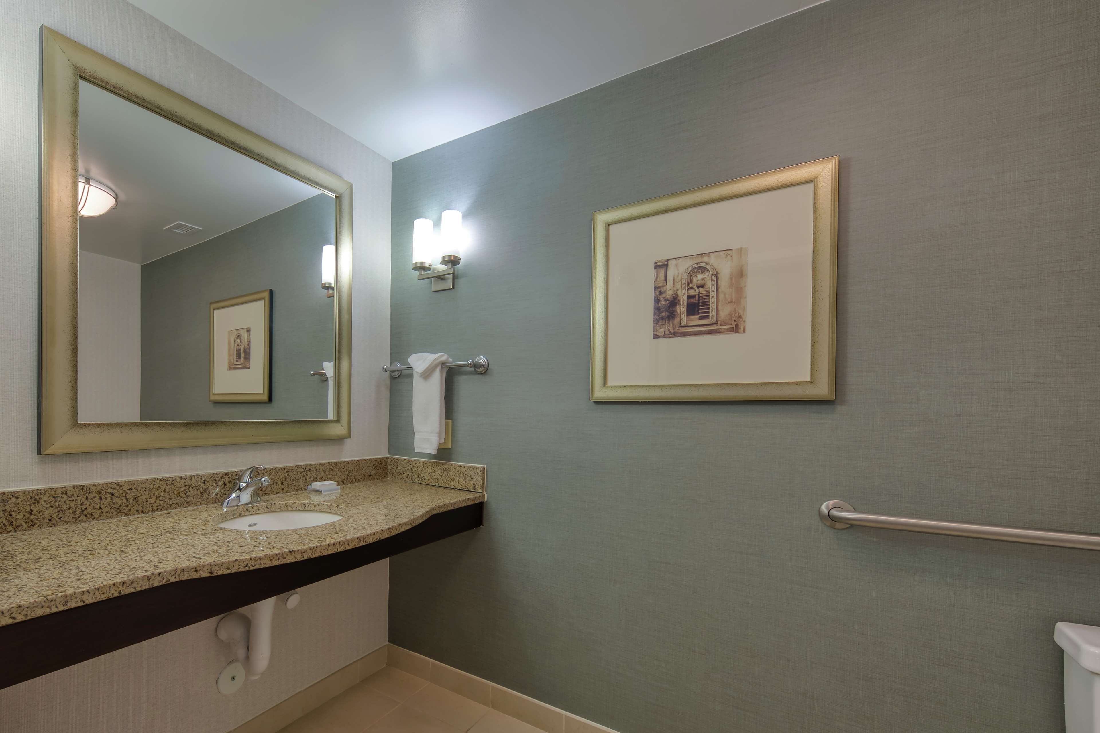 A bathroom with a sink, mirror, towel rack, and framed artwork on the wall.