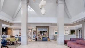 A spacious lobby with a central food kiosk, seating areas, and a high ceiling with hanging lights. - Hilton Garden Inn Durham Southpoint (Durham)