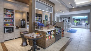 A modern hotel lobby with a coffee station, snack bar, and a view of the outside. - Hilton Garden Inn Durham Southpoint (Durham)