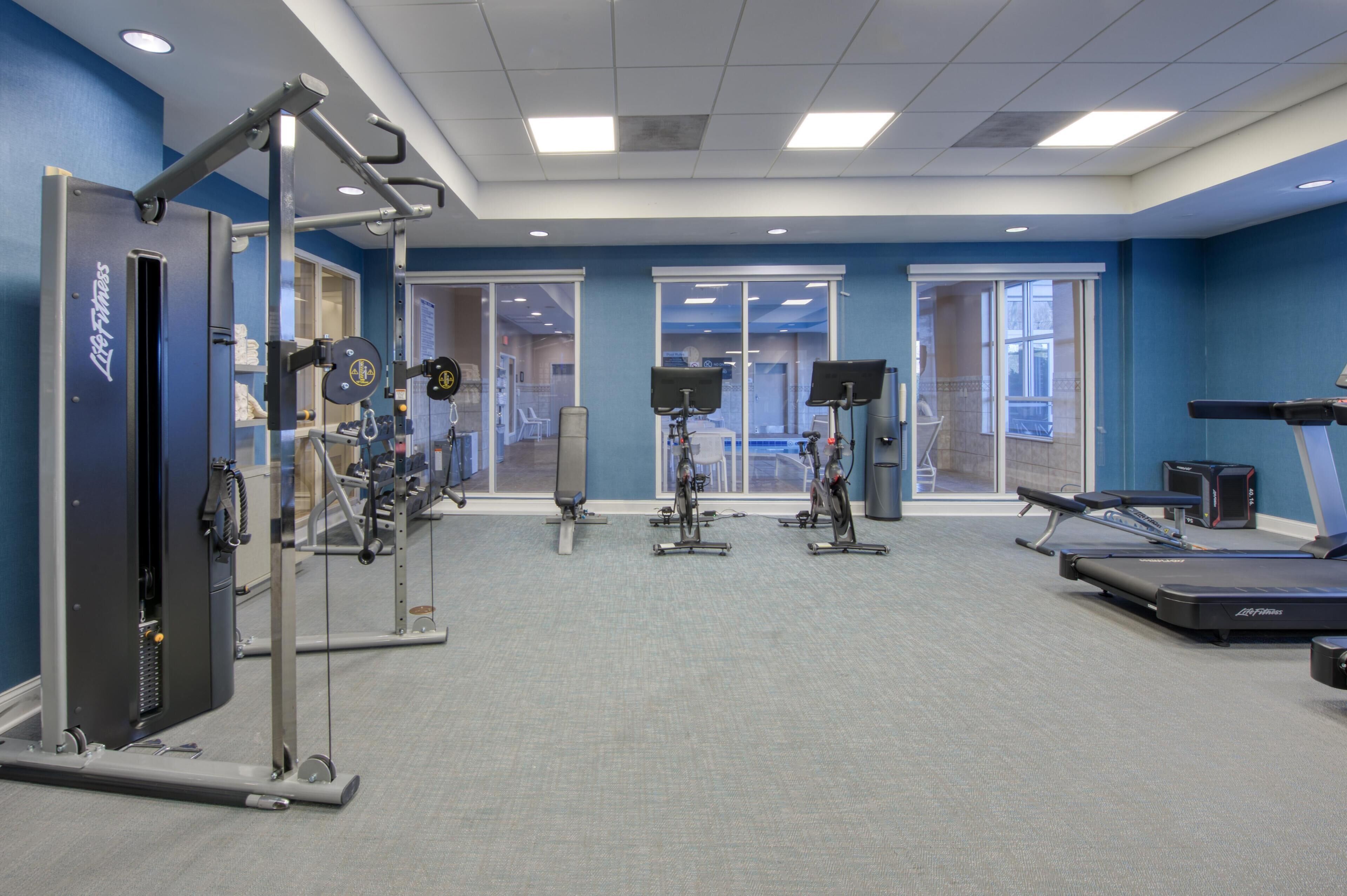 A gym with exercise equipment, large windows, and a blue wall.