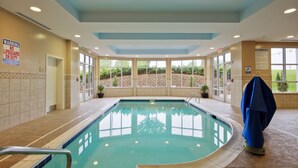 An indoor swimming pool with clear glass walls, a tiled floor, and a blue ceiling. - Hilton Garden Inn Durham Southpoint (Durham)
