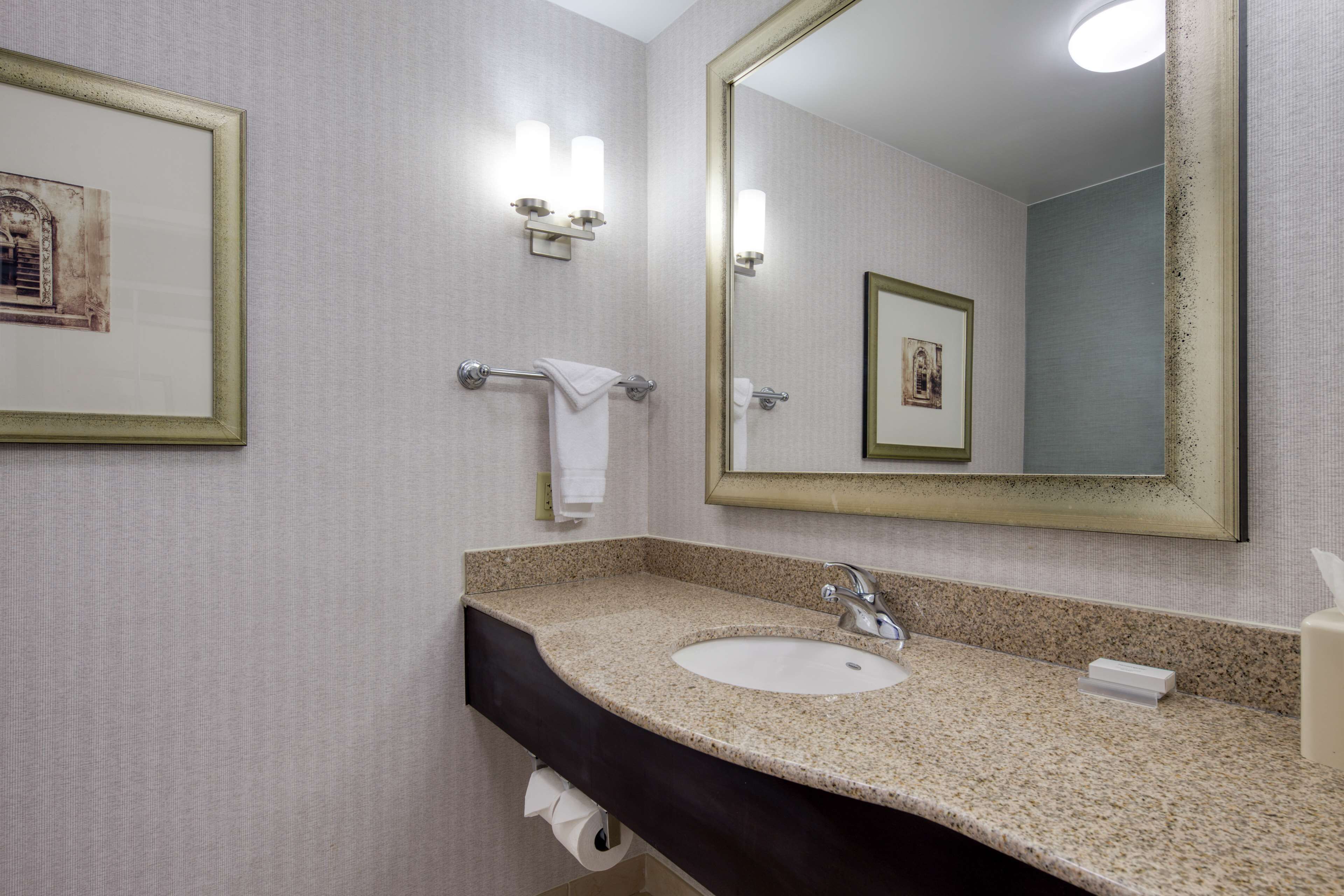 A bathroom with a granite countertop sink, a large mirror, and two wall-mounted light fixtures.