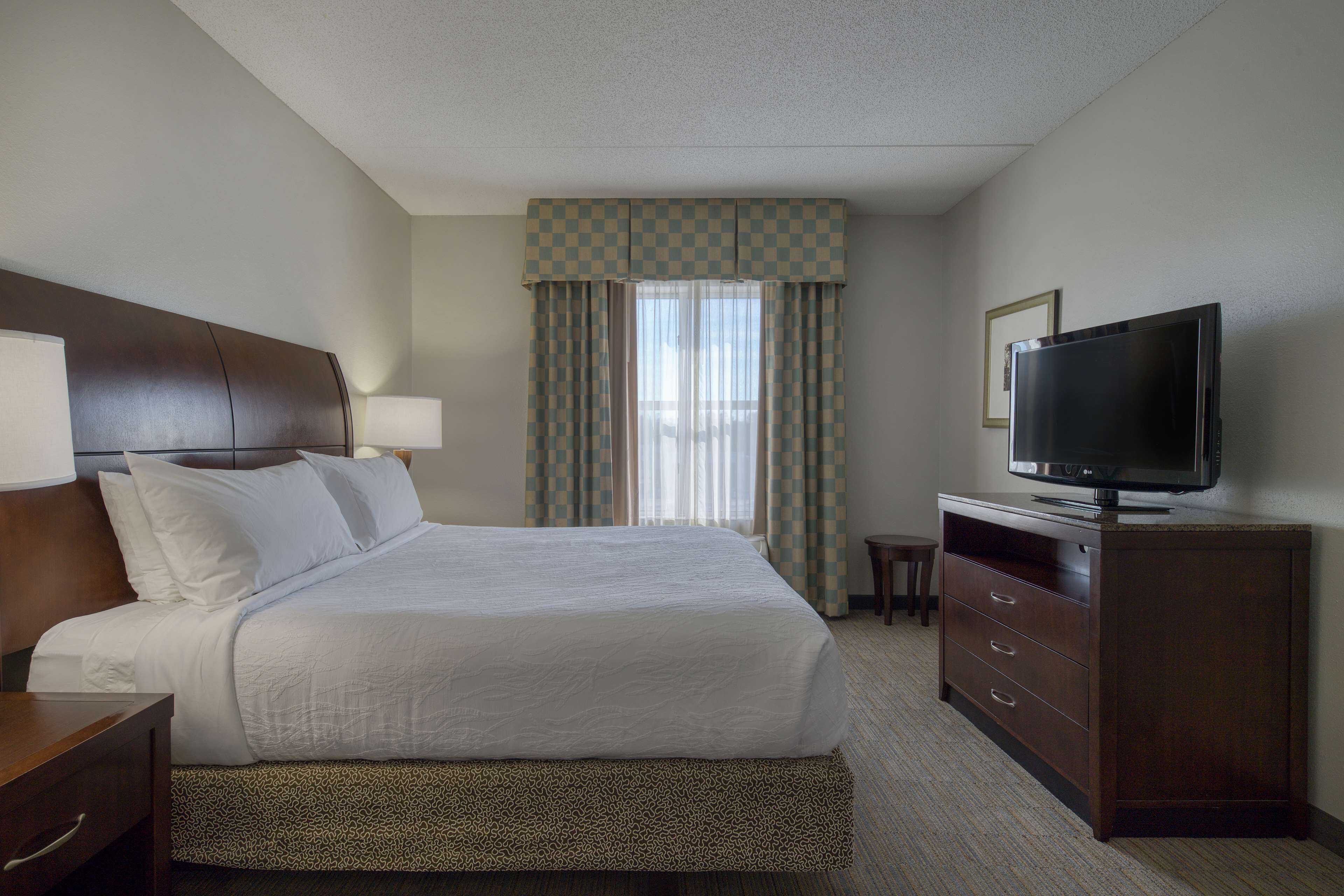 A hotel room with a large bed, a television on a wooden dresser, and a window with curtains.