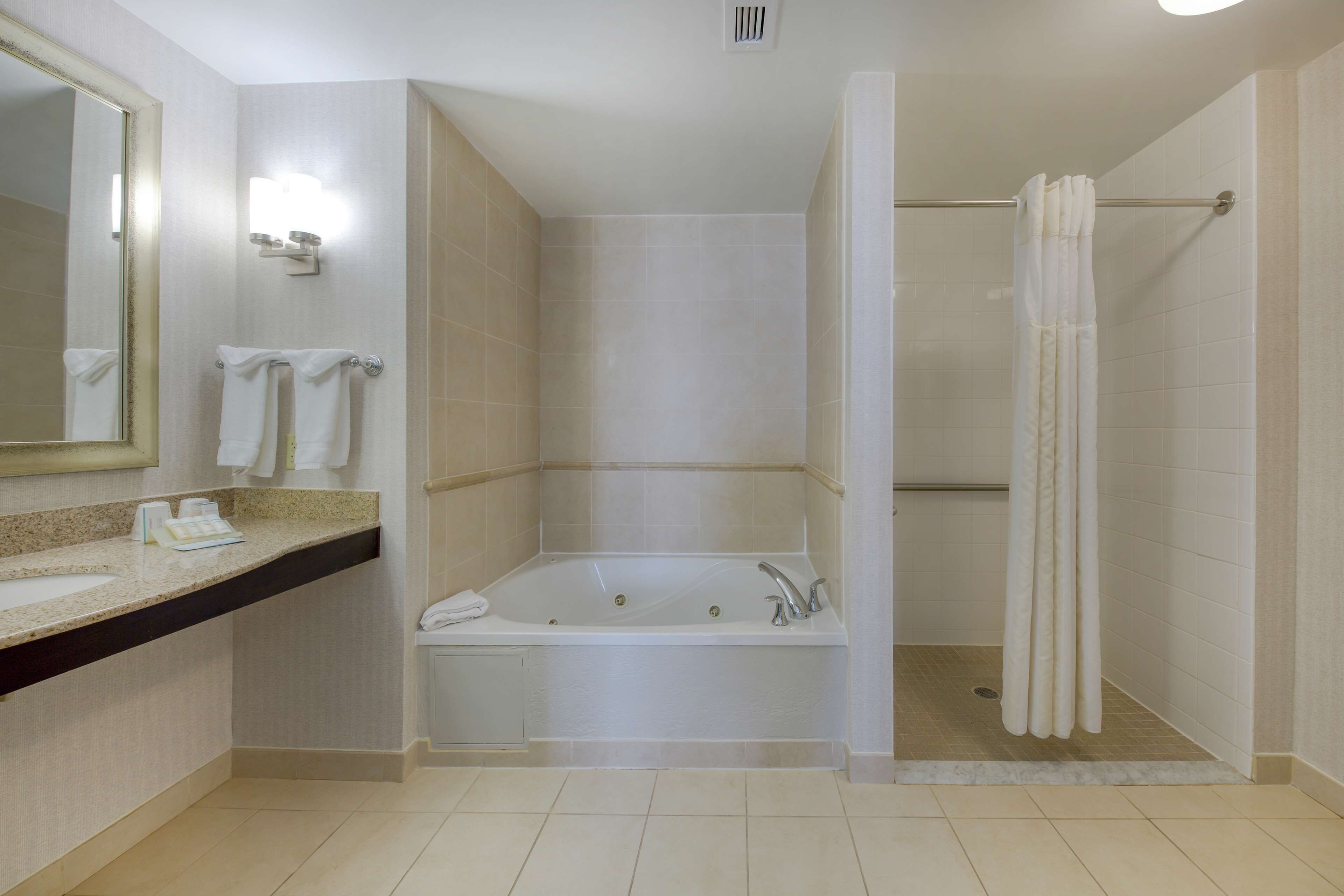 Un baño moderno con una bañera grande, zona de ducha y tocador con espejo y toallero.