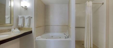 Un baño moderno con una bañera grande, zona de ducha y tocador con espejo y toallero.