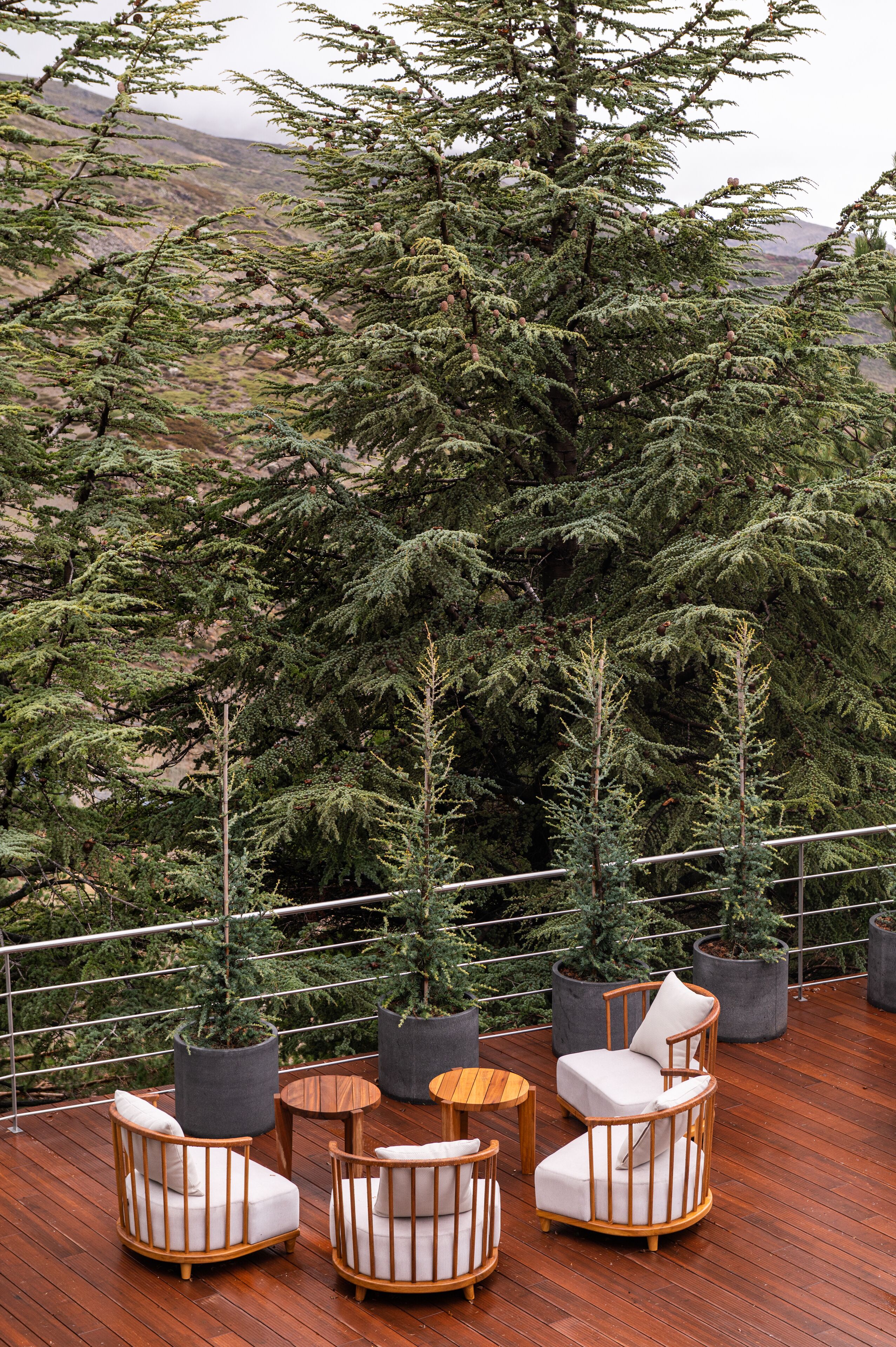 A wooden deck with outdoor seating and potted plants, overlooking a mountainous landscape.