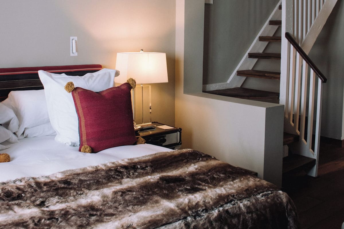 Una habitación de hotel con una cama, una mesita de noche con lámpara y una escalera.