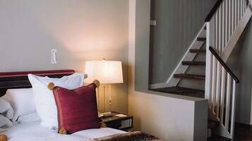 Una habitación de hotel con una cama, una mesita de noche con lámpara y una escalera.