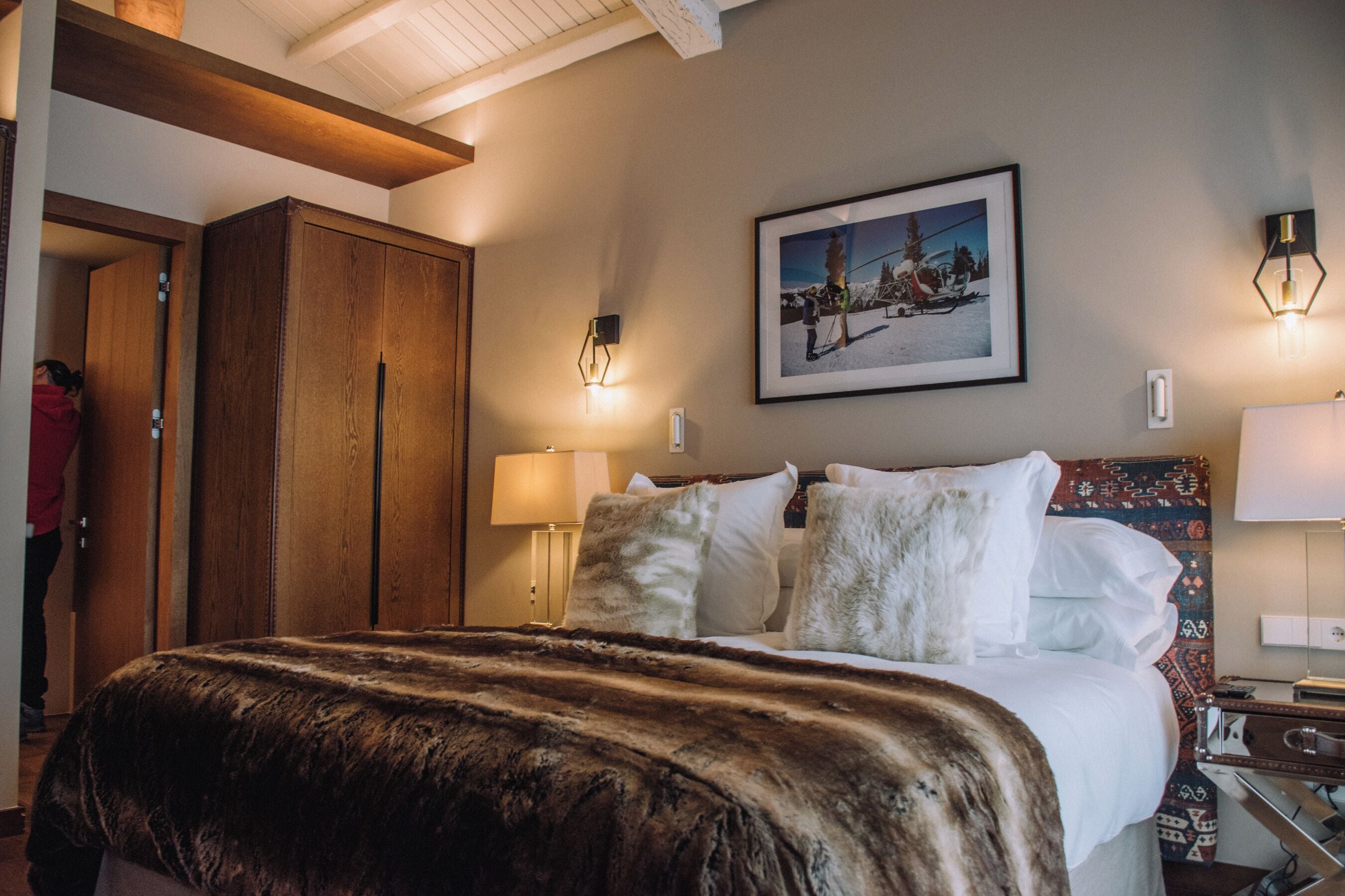 Habitación de hotel con una cama grande, un armario de madera, un cuadro enmarcado en la pared y dos lámparas fijadas a la pared.