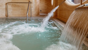 A wooden interior with a hot tub, metal railings, and a window.