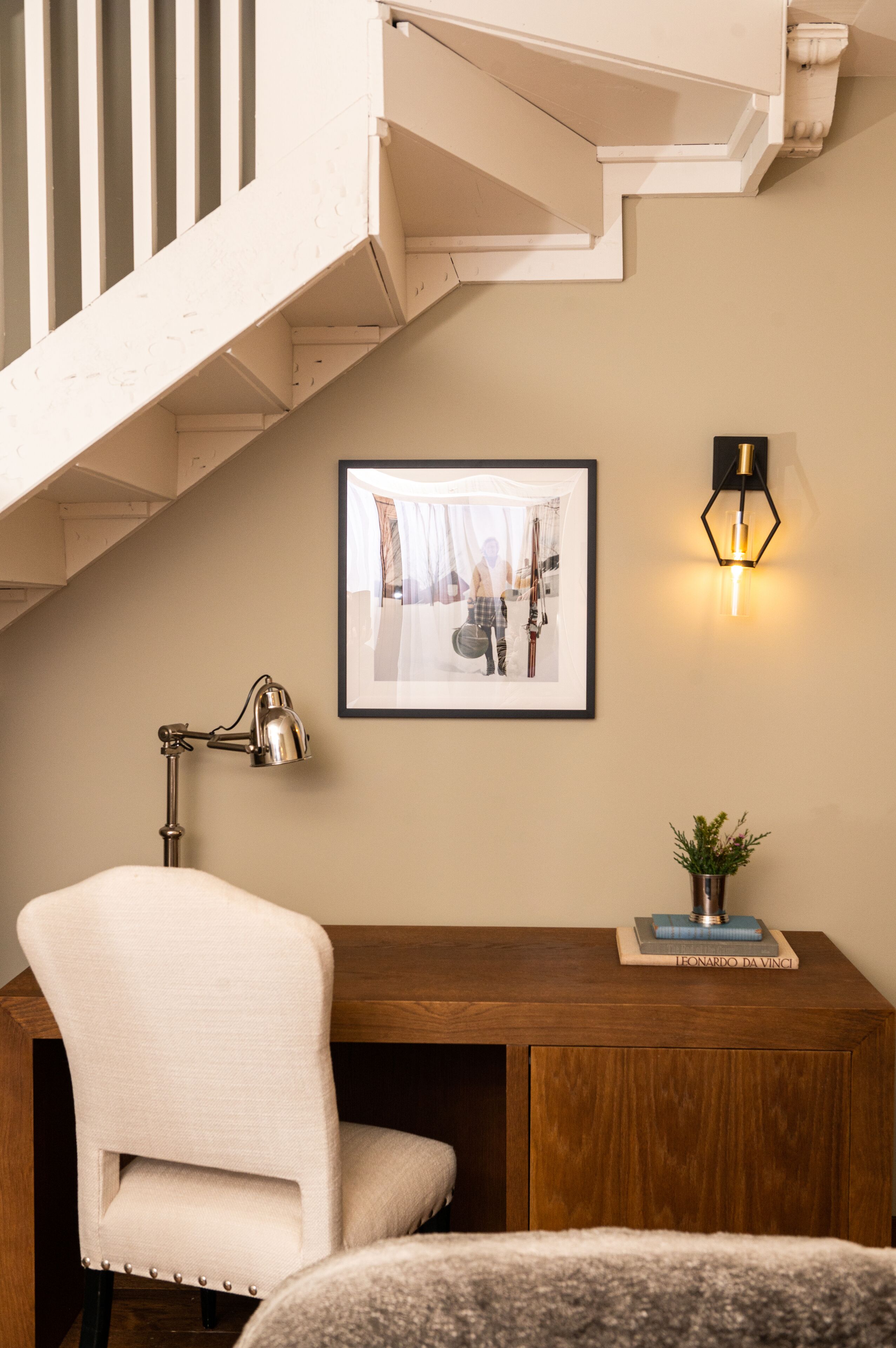 Un escalier avec une rampe blanche, un tableau encadré au mur, un bureau avec une lampe et une petite plante.