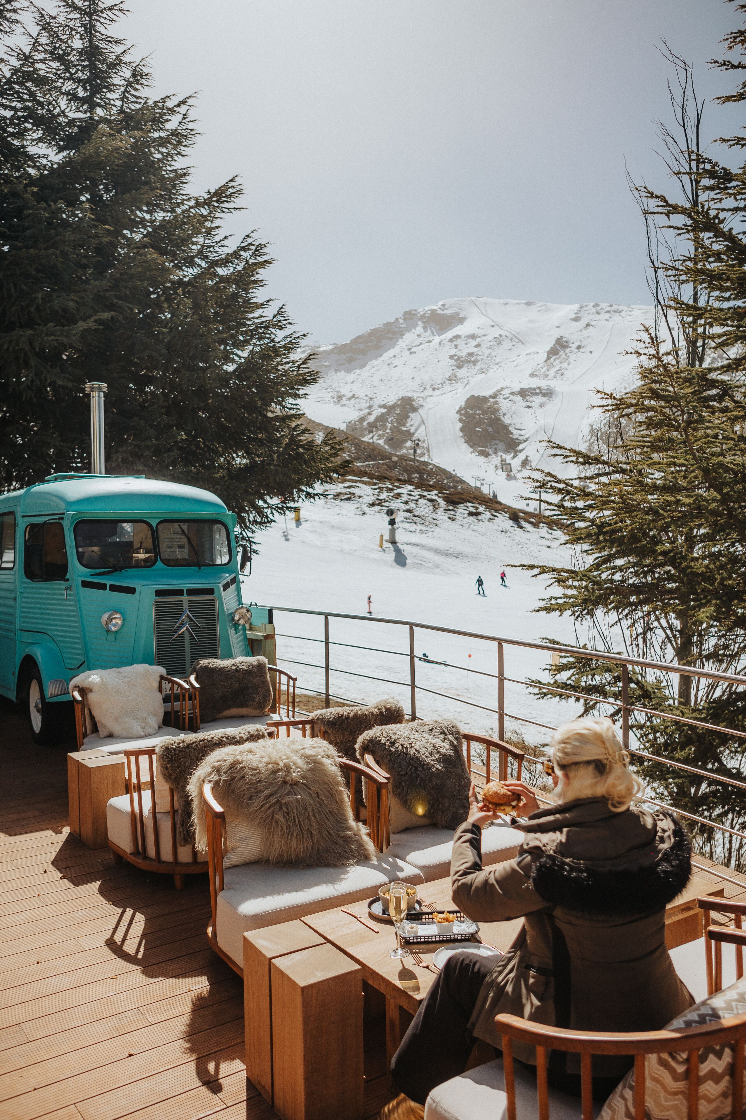 Un coche antiguo color turquesa estacionado en una terraza de madera con vista a una montaña nevada.