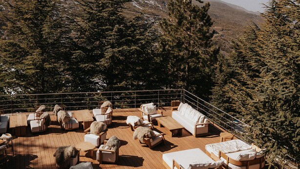 A wooden deck with outdoor seating and a view of snow-capped mountains and evergreen trees.