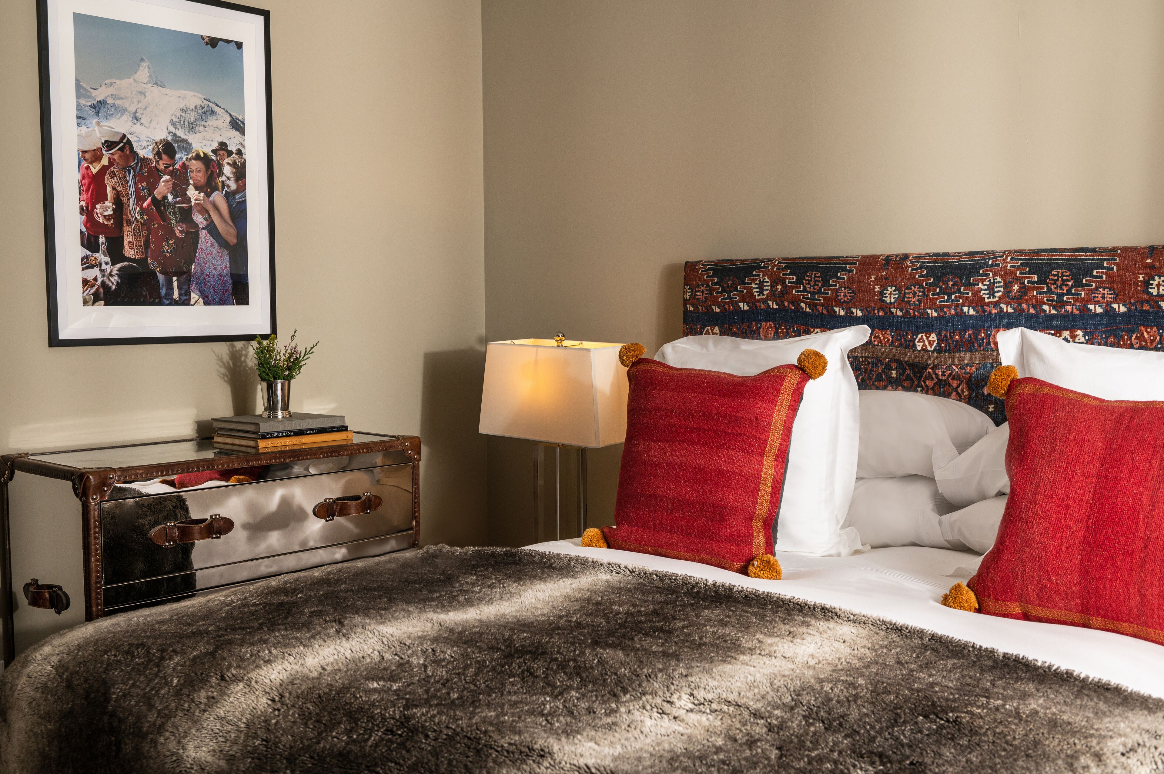 Una habitación de hotel con una cama, una mesita de noche con lámpara, una fotografía en el marco en la pared y una maleta en el suelo.