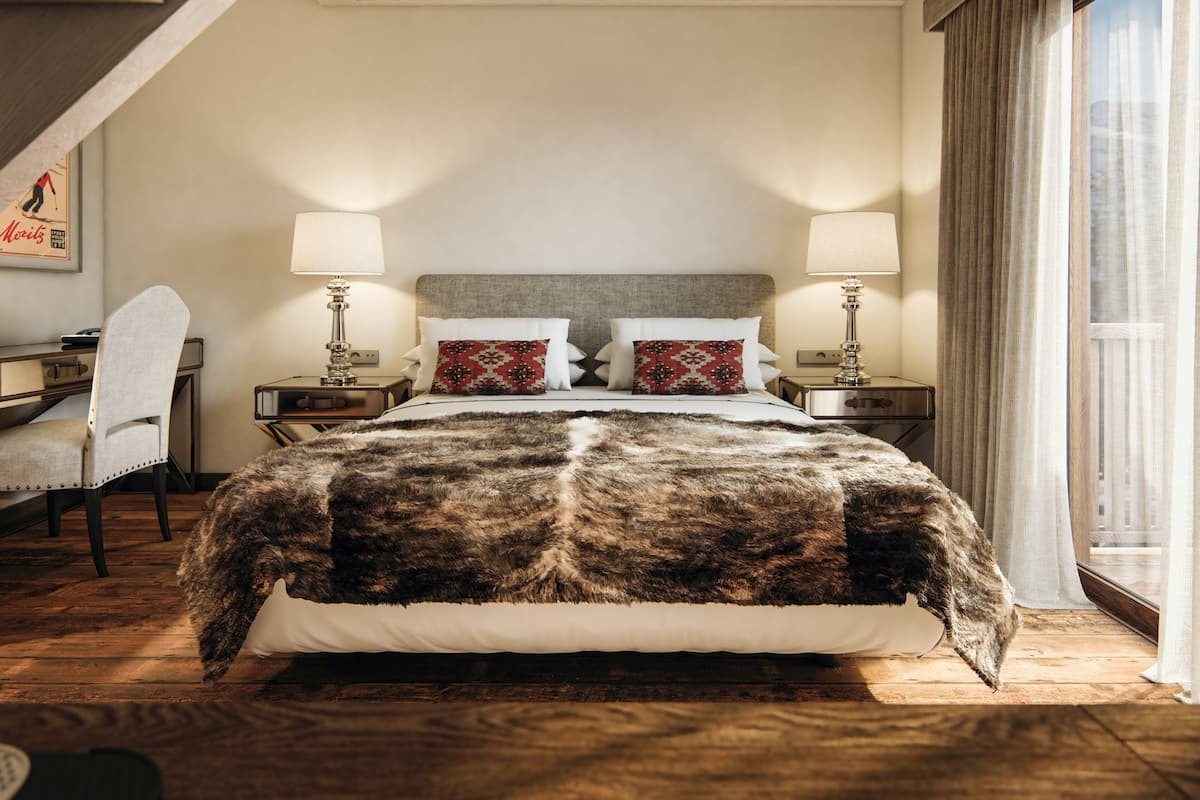 Habitación de hotel con una cama grande, dos mesitas de noche con lámparas, una silla, un escritorio y una ventana con cortinas.