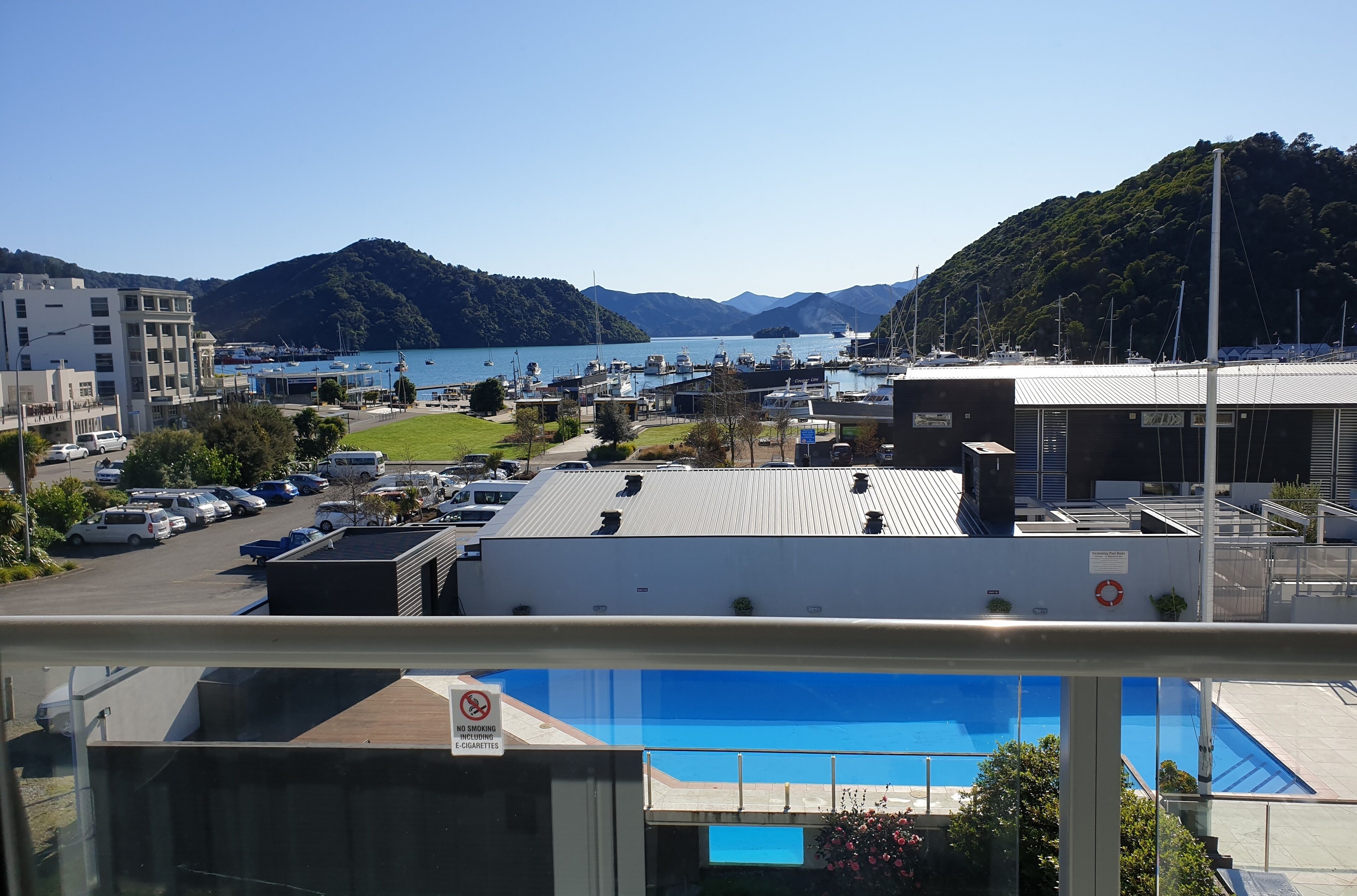 Vue d’une marina avec des bateaux, une piscine et un bâtiment sur lequel est affiché un panneau indiquant qu’il est interdit de fumer.