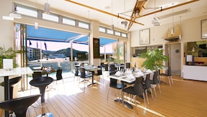 Un ristorante moderno con pavimento in legno, tavoli e sedie neri e bianchi. Ampie finestre offrono vista sull'esterno.